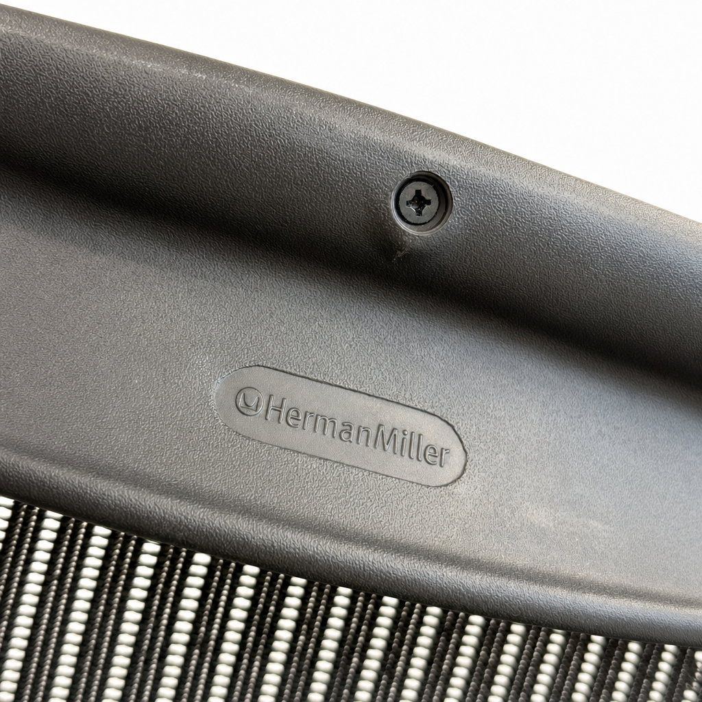 Herman Miller Logo auf schwarzem Kunststoffrahmen eines ergonomischen Bürostuhls mit anthrazitfarbenem Netzgewebe.