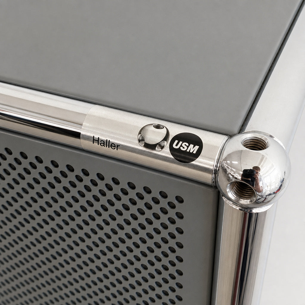 Mittelgraues USM Haller Highboard mit perforierten Schallschutz-Elementen und charakteristischem Chrom-Kugelgelenk.