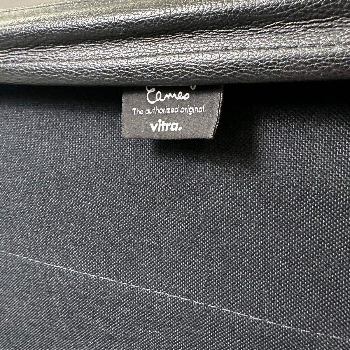 Detailaufnahme des schwarzen Lederbezugs und Vitra Eames EA 219 Labels am polierten Aluminiumstuhl